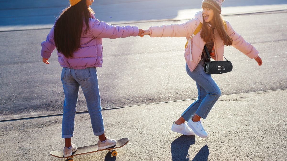Girls holding hands skateboarding carrying speaker
