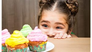 A little girl peers over the a countertop at a cupcake 