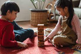 Two children sitting in the living room playing Jenga with wooden blocks